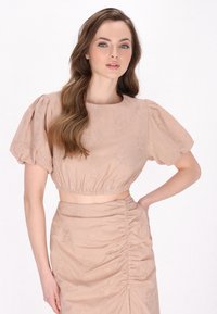 Blush pink to-delt outfit bestående af en cropped top med puff ærmer og blomsterbroderi, stylet med en rynket nederdel. Glat stofstruktur.