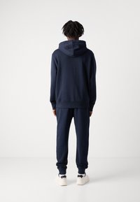 Sweatshirt com capuz azul-marinho emparelhado com calças de jogging correspondentes; conta com um corte solto, punhos canelados e faixa elástica na cintura para conforto.