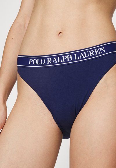 Tumedat sinine puuvillane string, millel on logo vöö, sisaldades valget teksti ja helesiniseid aktsente. Pehme tekstuur ja sobiv disain, nähtavad mustrid puuduvad.