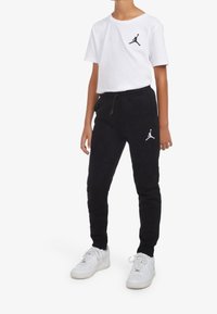 Vit t-shirt med svart Jordan-logga, ihopparad med svarta joggarbyxor som har en matchande logga. Båda plagg är gjorda av mjukt material.