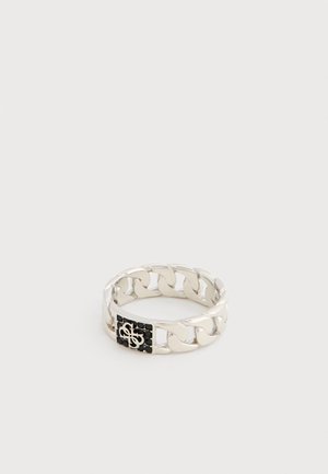 Bague en maillons de chaîne argentée avec un détail rectangulaire noir présentant un monogramme blanc entrelacé, sur un fond uni.