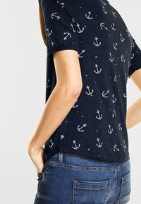 Marinblå kortärmad t-shirt med ett upprepat ankarmönster i vitt. Tillverkad av ett texturerat tyg med en avslappnad passform och sidofickor.