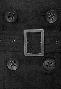 Schwarzer Wollmantel mit einem doppelreiherigen Design, vier runden schwarzen Knöpfen und einer rechteckigen Metallbuckle-Akzent. Glatte Textur.