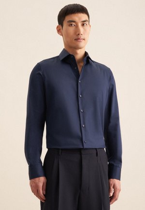 Marine knoopshirt van gladde stof, met een verspreide kraag, lange mouwen en subtiele textuur, gecombineerd met op maat gemaakte broeken.