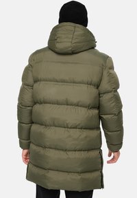 Olivengrøn pufferjakke med hætte, med en quiltet design, mellemlang længde og lynlås i siderne, parret med en sort hue.
