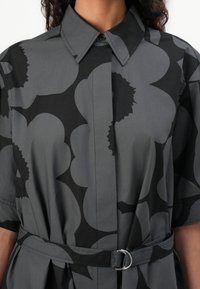 Grey shirt with large black floral pattern, button-down collar, short sleeves, and a matching belt with a silver ring buckle. Smooth texture.