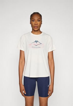 Μπεζ κοντομάνικη μπλούζα με γραφικό βουνό και κείμενο· συνδυασμένη με ναυτικό σορτς ποδηλασίας, που αναδεικνύει μια λεία υφή και άνετη εφαρμογή.