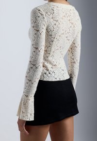 Top a maniche lunghe in pizzo con motivo floreale di colore avorio, abbinato a una gonna nera aderente. Presenta maniche a campana e una silhouette aderente.