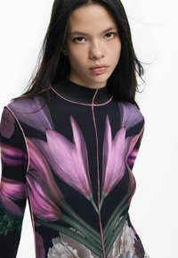 Keha järgnev pikkade varrukatega särk tumeda taustaga, millel on erksad lilla lillemustrid ja roosa kontrastõmblus kaeluse ääres.