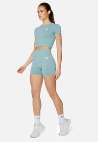 Světle modrý sportovní set skládající se z krátkého rukávu crop topu a šortek s vysokým pasem, vyrobený z hladké látky s malým bílým logem.