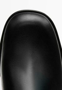 Chaussure noire en cuir au toucher lisse, forme arrondie à l'avant et coutures discrètes le long du bord. Sans accents ni éléments métalliques visibles.