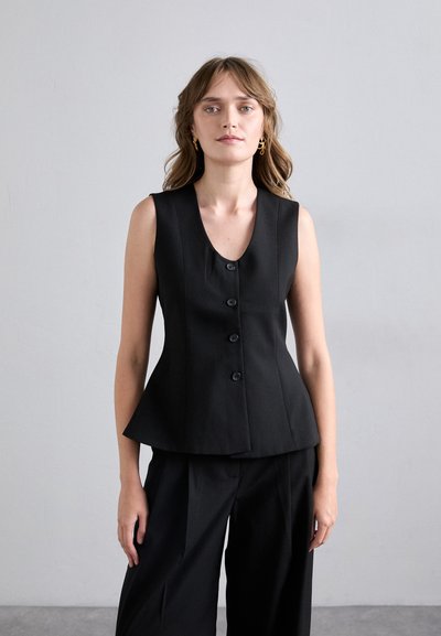 Gilet nero senza maniche, sagomato, con scollatura a V, caratterizzato da cinque bottoni frontali e orlo peplum, abbinato a pantaloni neri a gamba larga.