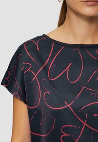 Navyblaues Kurzarmoberteil mit rotem Herzmuster und Schriftzügen. Der Ausschnitt ist rund, mit einer glatten Textur und lockerer Passform.