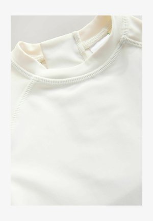 Vitt sportlinne med rund halsringning, slät textur och kontrasterande sömmar. Designen inkluderar raglanärmar för full rörelsefrihet.