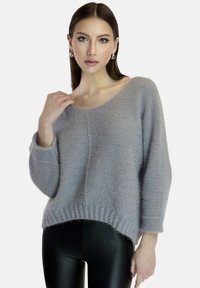 Maglione grigio chiaro lavorato a maglia con una vestibilità morbida, scollatura ampia e orlo a coste. Tessuto morbido con spalle scese, indossato sopra leggings neri lucidi.