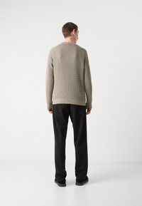 Grau gestrickter Pullover mit strukturiertem Muster, Rundhalsausschnitt, langen Ärmeln und gerippten Bündchen, kombiniert mit schwarzen Hosen und dunklen Schuhen.