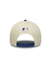Καπέλο μπέιζμπολ, μπεζ ύφασμα, μπλε πλαστικό κούμπωμα snapback, κεντημένο λογότυπο MLB στο πίσω μέρος, στρογγυλεμένο σχήμα, ομαλή υφή.