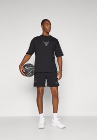 Mustat lyhythihaiset paidat ja shortsit, joissa on Chicago Bulls -logo, valmistettu teksturoidusta kankaasta. Yhdistetty valkoisiin urheilukenkiin ja pitelee koripalloa.
