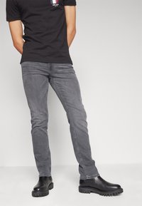 Jeans grises de corte ajustado, con cinco bolsillos y costuras sutiles, combinados con botas negras hasta el tobillo con suelas texturizadas.