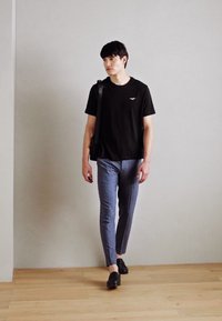 Zwarte korte mouwen t-shirt gecombineerd met lichtblauwe slim-fit broek en zwarte nette schoenen. Man die binnen loopt met een schoudertas.