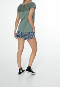 Grøn t-shirt med tekstureret blonde ryg, parret med marineblå shorts med hvidt blomstermønster og sorte høj-top sneakers.