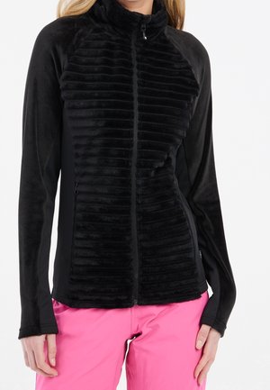 Femme portant une veste polaire noire à fermeture éclair intégrale avec un devant texturé et des manches unies, associée à un pantalon rose vif.