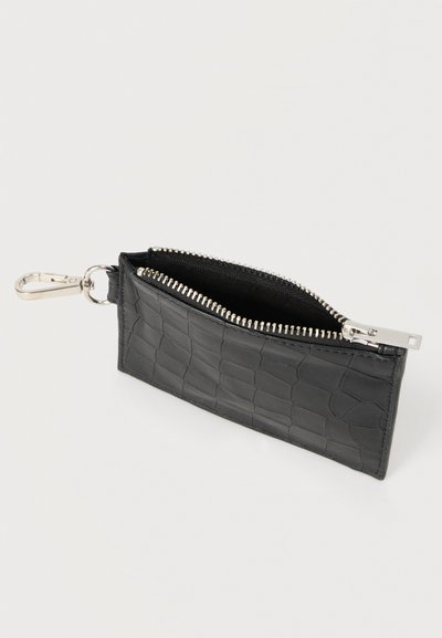 Μαύρο δερμάτινο πορτοφόλι με φερμουάρ και υφή κροκοδείλου, με ασημένια μεταλλικά στοιχεία και κλιπ για στερέωση. Το εσωτερικό είναι επενδυμένο με ύφασμα.