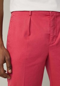 Rosa Hosen aus glattem Material, mit flachem Bund, seitlichen Taschen und tailliertem Schnitt. Subtile Falten unterstreichen das Design.
