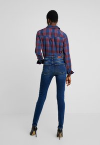 Camisa de cuadros roja y azul, jeans ajustados de mezclilla y zapatos de tacón negro. Enfoque en el cuello abotonado de la camisa y su diseño ajustado.