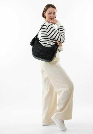 Sac en bandoulière noir tissé avec une forme arrondie et une finition texturée, doté d'un fond en cuir et d'un accent en pompon, porté sur un pull rayé.