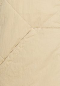 Beige kviltat tyg med ett diagonalt sömnads mönster, slät textur och subtil lyster. En detaljerad, precis sömnad förbättrar designen.