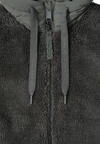 Hřejivá fleecová bunda v tmavě šedé barvě, s měkkou texturou, zipovým zapínáním a dekorativními šňůrkami s reliéfním textem.