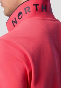 Polo shirt rosa con colletto alto caratterizzato dalla scritta "NORTH" in grassetto nero sul colletto. Tessuto texturizzato con una finitura liscia.