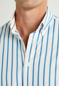 Camisa de botones a rayas con franjas verticales en azul y naranja sobre un fondo blanco; tela de algodón con un diseño de cuello clásico.