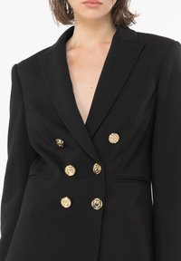 Black double-breasted blazer with gold buttons, sharp lapels, and a deep V-neck. Tailored fit with shoulder pads and side pockets.