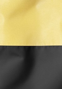 Deux sections de tissu, l'une jaune brillant en haut et l'autre noire matte en bas, se rencontrent à une couture propre et droite. Les matériaux semblent lisses et légers.