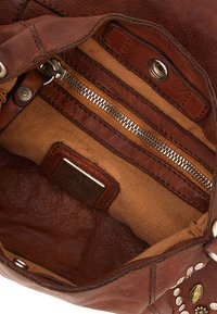 Interno di una borsa in pelle marrone con fodera in tessuto beige, dotata di una tasca con cerniera e borchie decorative lungo il bordo.