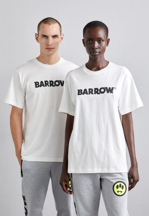 T-shirt bianche in cotone con logo nero "BARROW", abbinate a pantaloni della tuta grigi con un design di faccina sorridente verde e accenti neri.