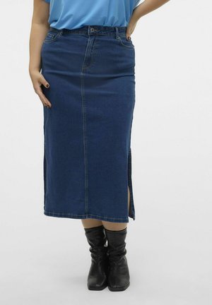 Jupe midi en denim bleu foncé avec une coupe droite, des fentes latérales et des détails cousus. Associée à des bottes noires montantes.