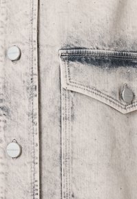 Tissu en denim gris clair avec une poche avant cousue et des boutons argentés gravés "ALLSAINTS" sur un vêtement.