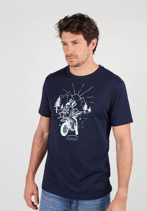 T-shirt en coton bleu marine avec un imprimé graphique représentant un cycliste sur une moto devant un paysage de montagne et de soleil. Manches courtes, col rond.