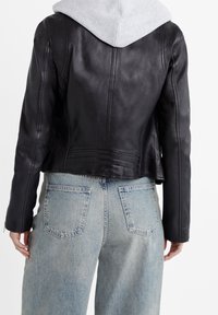 Schwarze Lederjacke mit kurzem Schnitt, verfügt über eine glatte Textur und Rückennaht-Details, kombiniert mit hellblauen Jeans aus Denim.