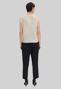 Helle beige Kurzarmbluse mit transparentem Yoke, kombiniert mit schwarzen weit geschnittenen Hosen. Transparenter Stoff an den Schultern, insgesamt entspannter Schnitt.