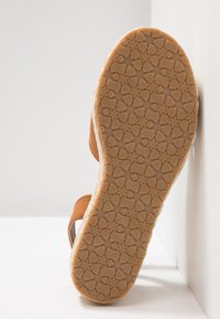 Sandale marron avec une semelle en caoutchouc texturée présentant un motif en forme d'étoile. Bride réglable pour un ajustement parfait. Vue de dessous mettant en évidence le dessin de la semelle.