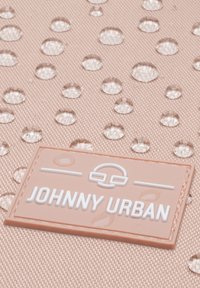 Vattentätt tyg i ljusrosa med upphöjda droppar. En vit rektangulär etikett med texten "JOHNNY URBAN" finns i det nedre vänstra hörnet.