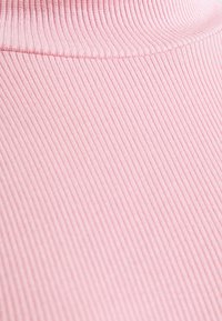 Růžová žebrovaná látka s měkkou texturou a vertikálními pruhy, s vysokým výstřihem a hladkým zakončením okrajů.