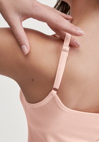 Light pink tank top with adjustable straps and a smooth texture, showing a close-up of the shoulder area and strap hardware detail.