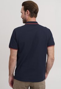 Mornarska polo majica s crvenim naglascima na ovratniku i rukavima. Kratki rukavi i opušteni kroj, izrađena od mekog, prozračnog materijala.