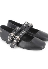 Zapatos Mary Jane de cuero negro con correas de doble hebilla, que cuentan con ojales plateados y puntas redondeadas sobre un fondo blanco.