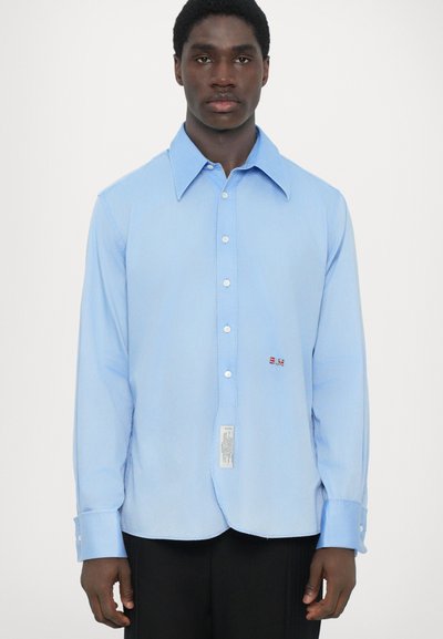 Lichtblauwe lange mouwen shirt met een puntige kraag, voor knoopsluiting en een klein rood geborduurd detail vlakbij de zoom. Gladde textuur.